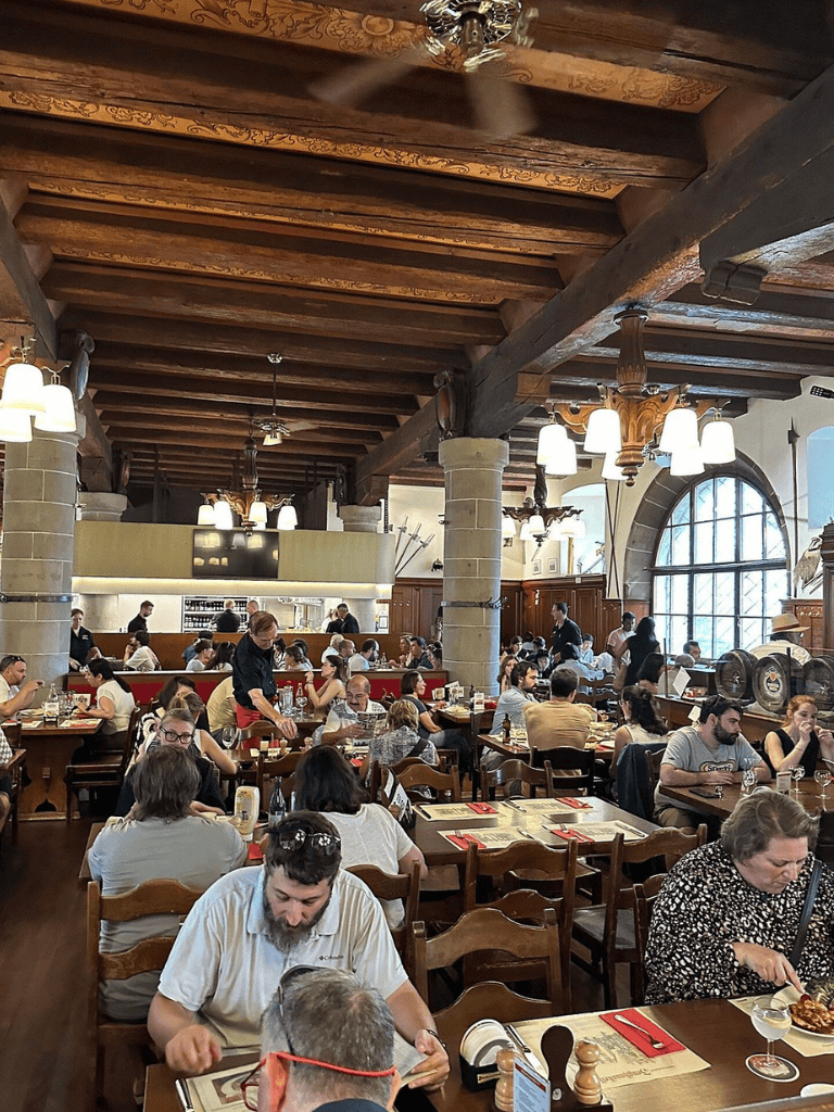 Doorway restaurant interior with wooden beams, large windows, and busy diners enjoying meals.