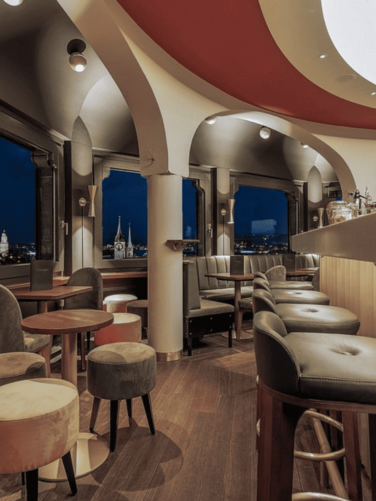 Cozy modern cafe interior with city skyline view at night, plush seating, and stylish decor, perfect for relaxing sessions.