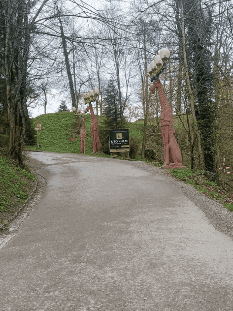 1. Tall wooden statues holding lamps on a sloped road in a wooded area.
