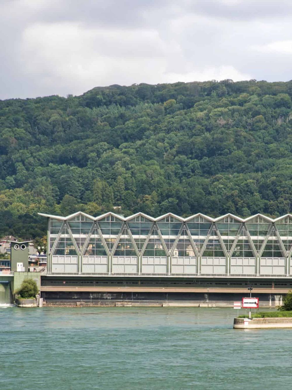 Modern riverside building with mountain backdrop, innovative architecture, and scenic water view.