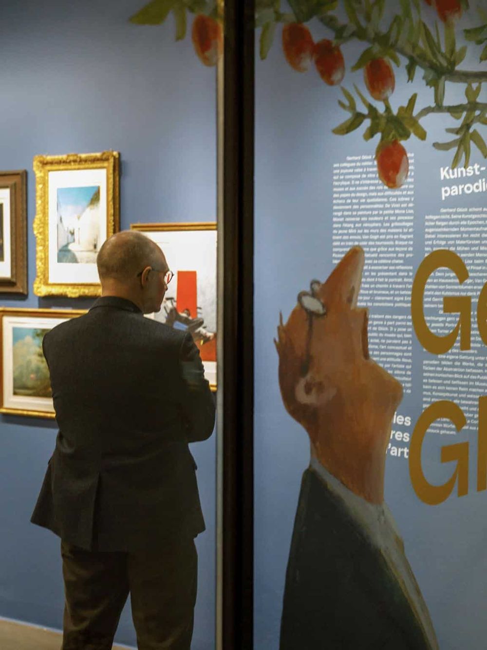 Colorful art gallery with framed paintings and informational panels on blue walls, visitor engaging with artwork.