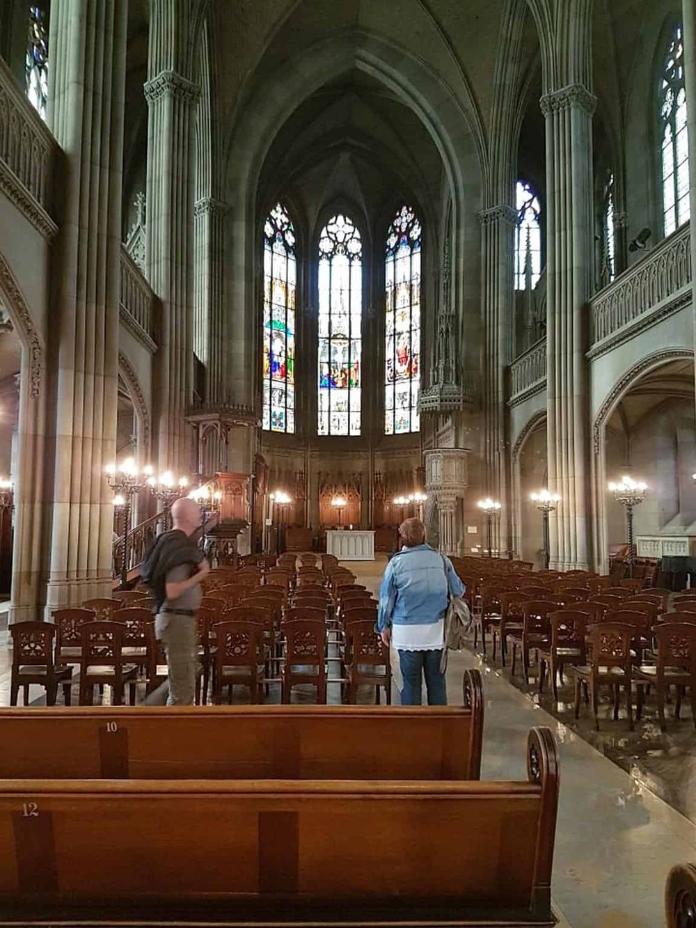 Ornate Gothic cathedral interior with stained glass windows and wooden pews, showcasing historic architecture and religious artistry.