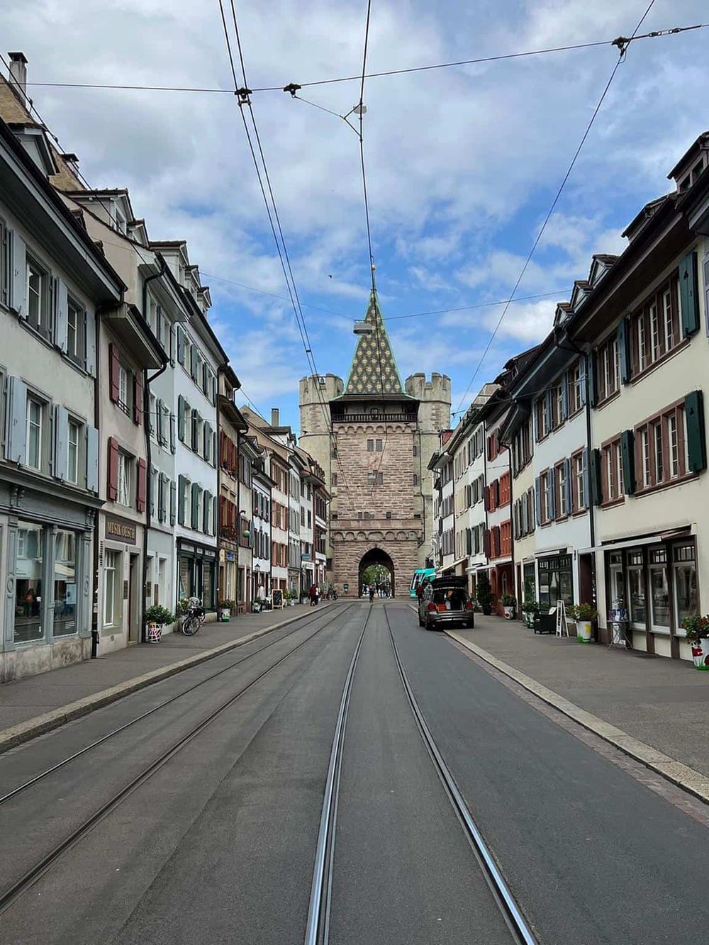 Colorful European street with historic gate and tram tracks, showcasing architecture and city life.