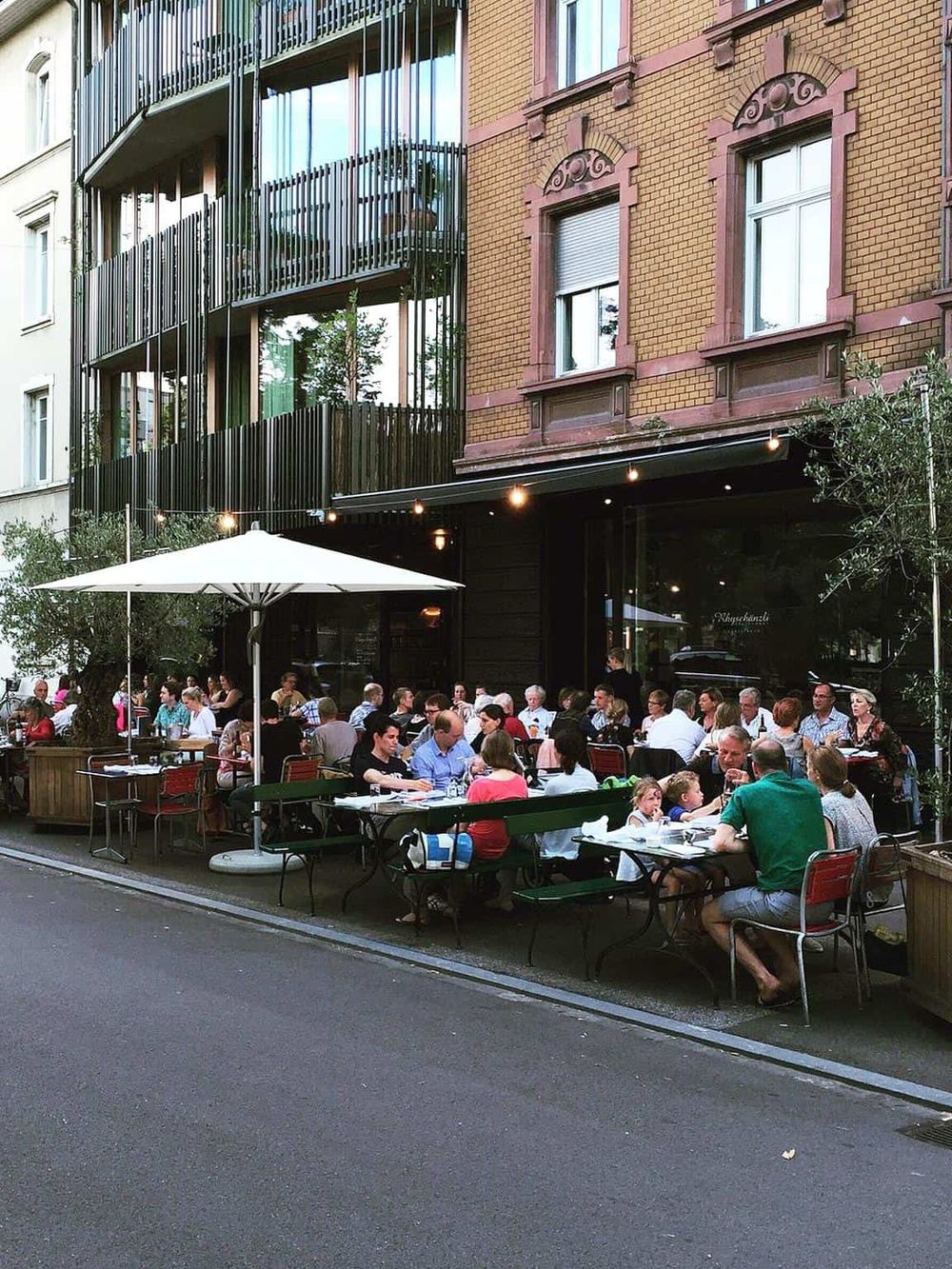 Outdoor dining restaurant with a vibrant crowd in front of a modern building.