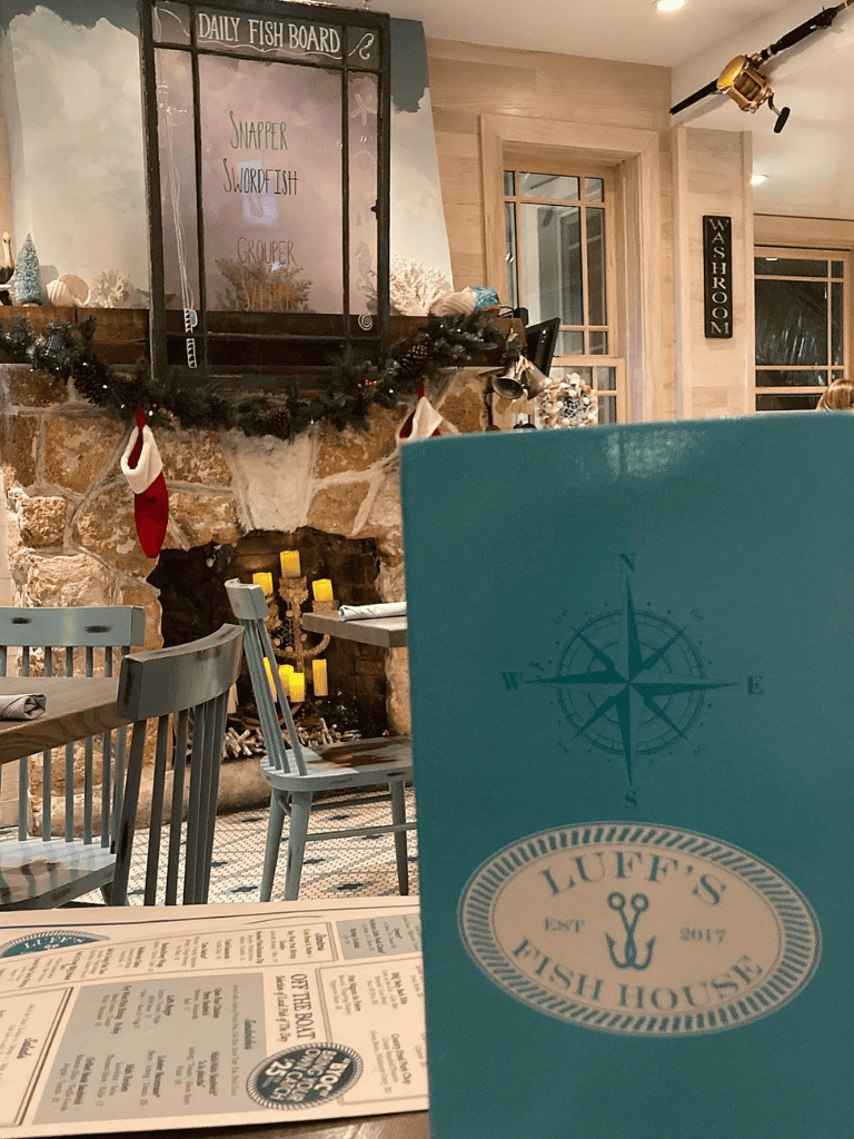 Cozy seaside fish house restaurant interior with fireplace, holiday decor, and nautical-themed menu.