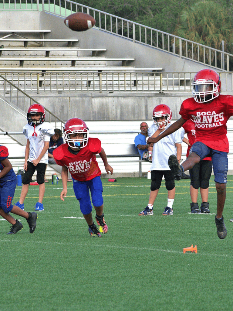 High school football practice with young players wearing red jerseys, practicing catching and running drills on the field.