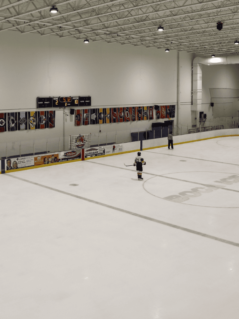 Empty hockey rink with player and referee, vibrant flags on wall, indoor ice sports facility for team hockey games.