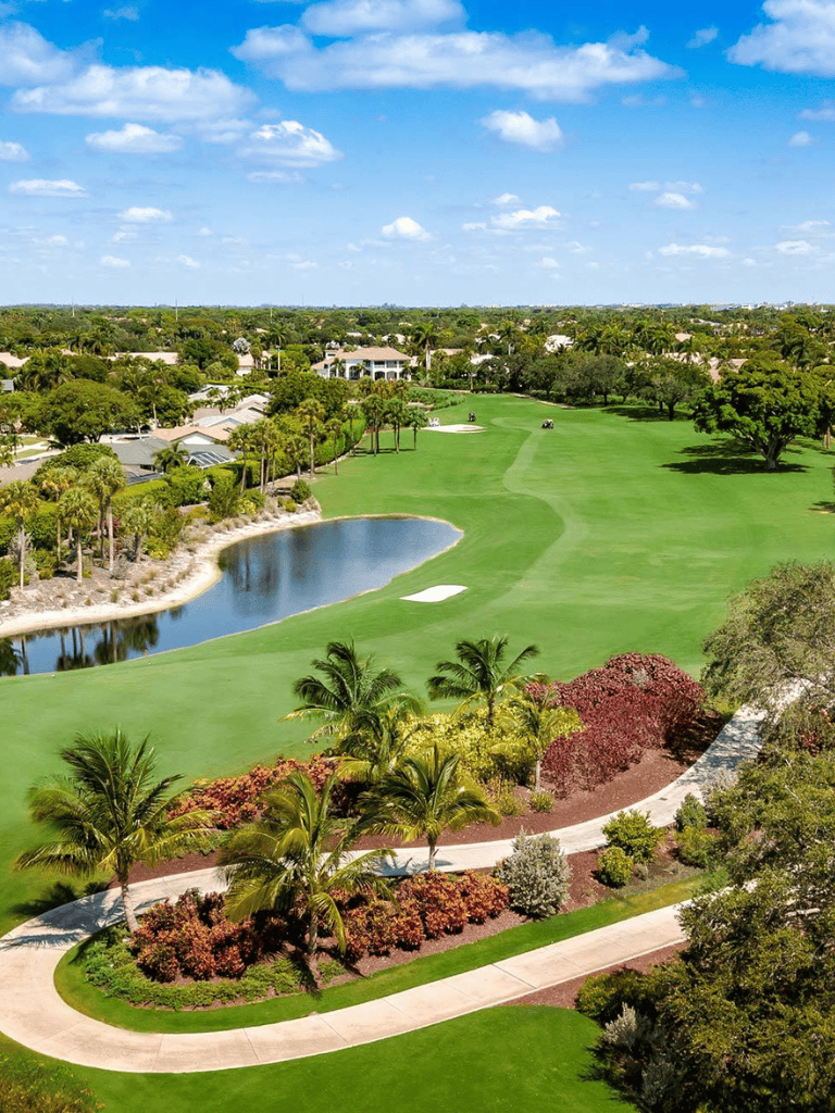 Gorgeous golf course with water hazard, lush greenery, and palm trees under a bright blue sky.