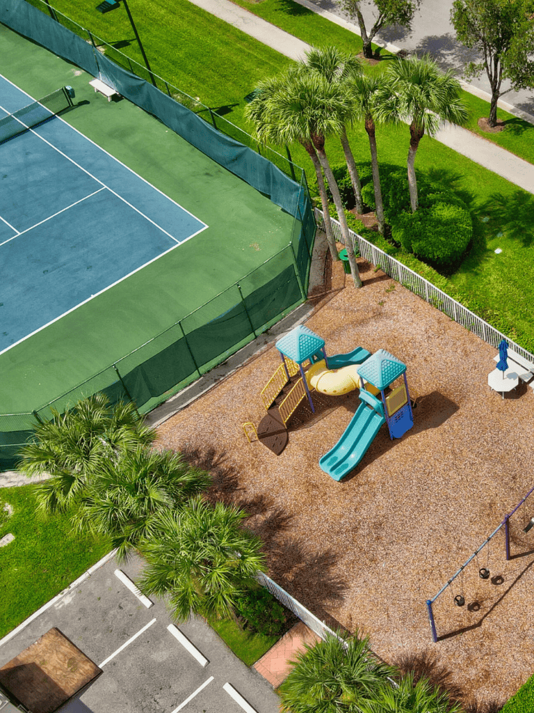 Vibrant tennis court and children’s play area with slides and swings surrounded by lush greenery.