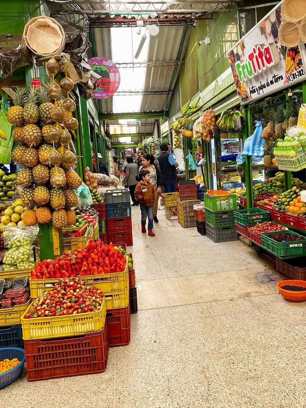 Colorful outdoor fruit market with fresh pineapples, strawberries, bananas, and other tropical fruits.