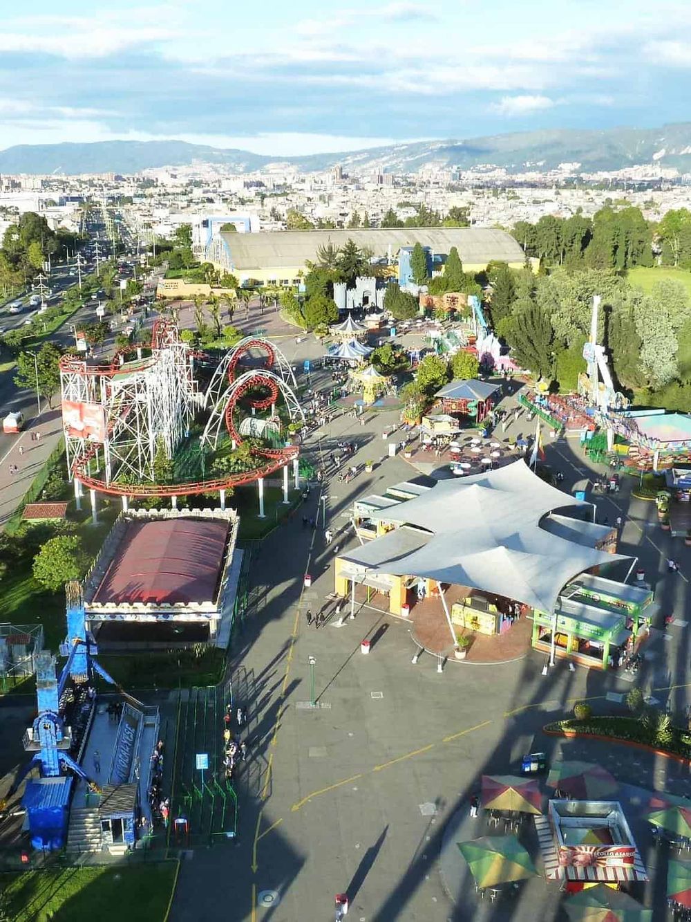 Vibrant amusement park with rides, tents, and attractions overlooking a scenic cityscape.