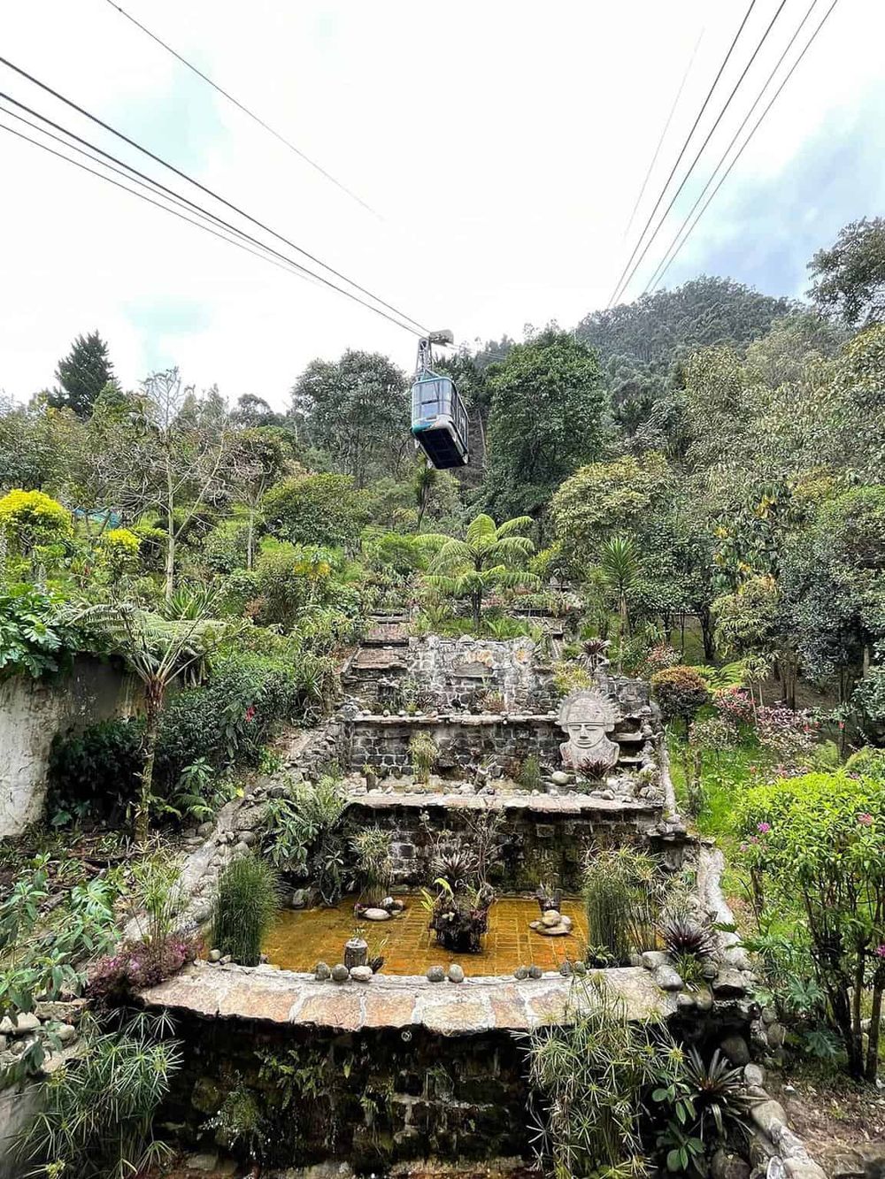 Cable car ride over lush garden waterfall natural landscape with greenery and rocky water feature.