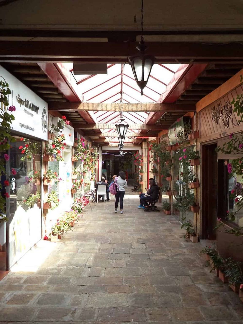Charming shopping arcade with hanging lanterns, vibrant flower pots, and boutique stores, offering a delightful browsing experience.