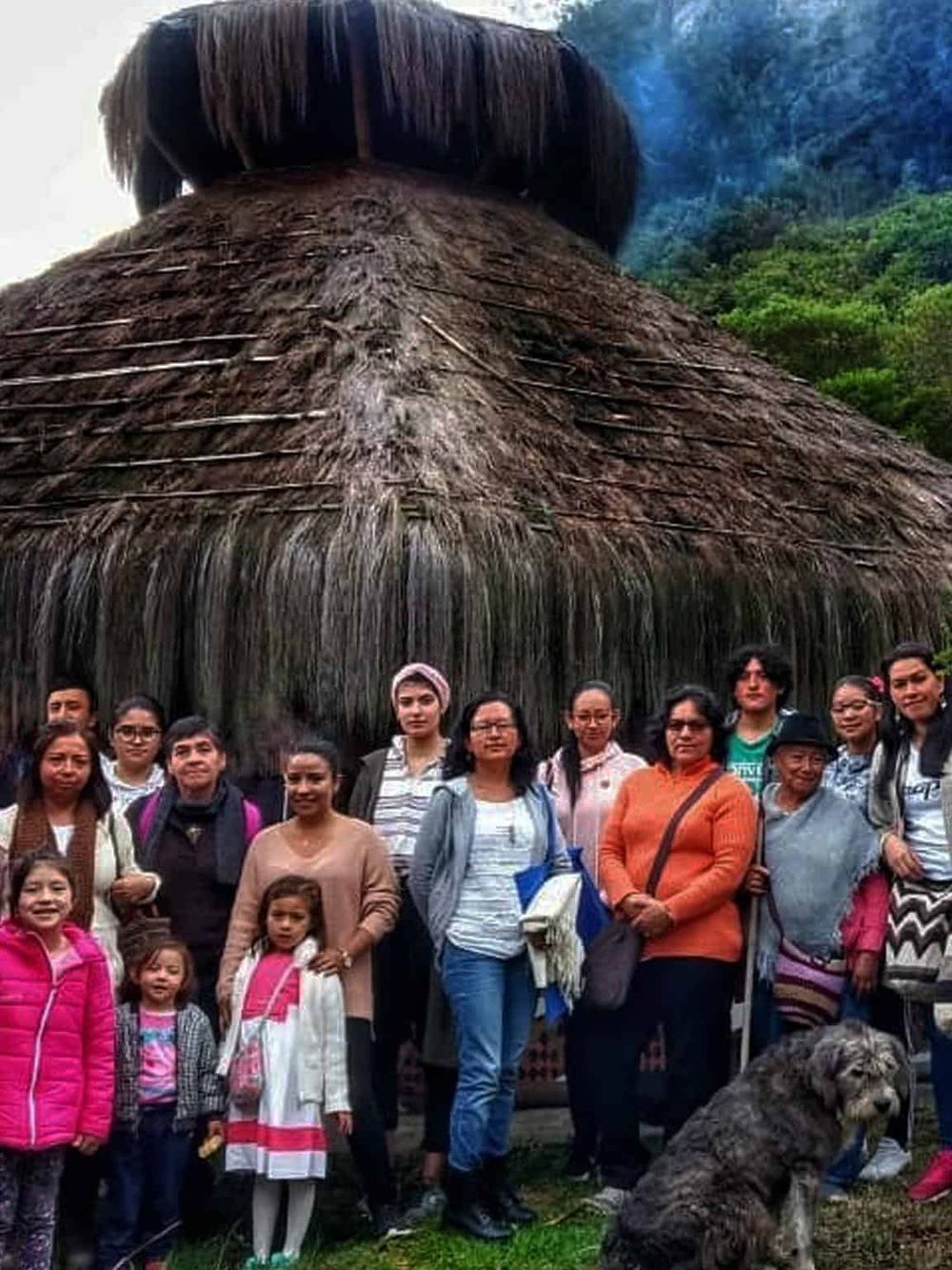 Colorful group of tourists posing in front of a large traditional thatched hut in a lush tropical setting, showcasing cultural tourism experiences.