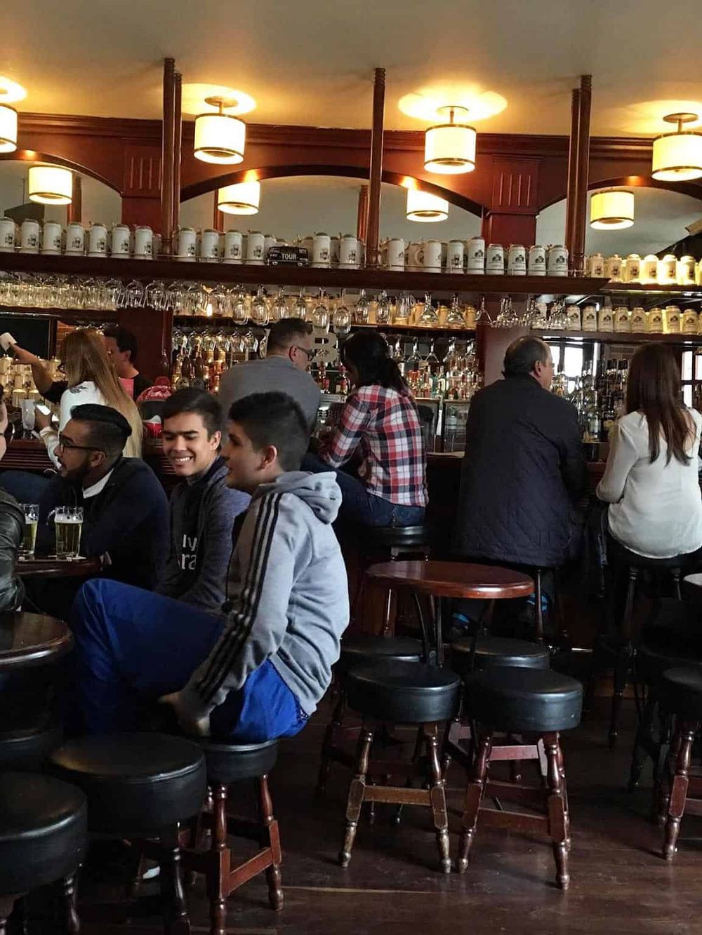 A lively pub scene with people enjoying drinks at a cozy bar, featuring warm lighting and wooden furniture.