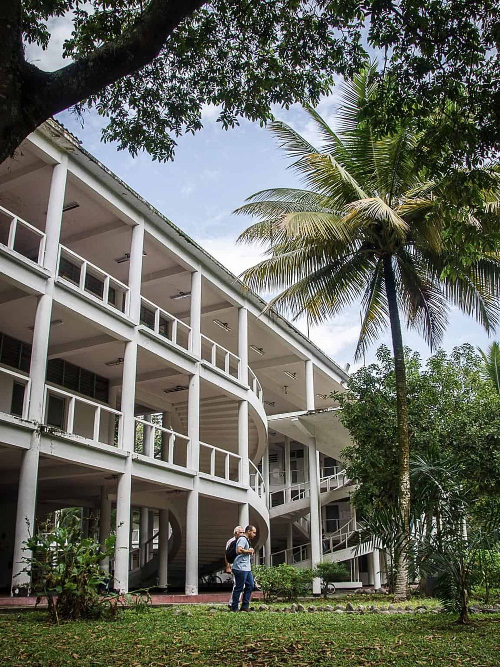 Modern multi-story building with outdoor walkways in a lush tropical environment.