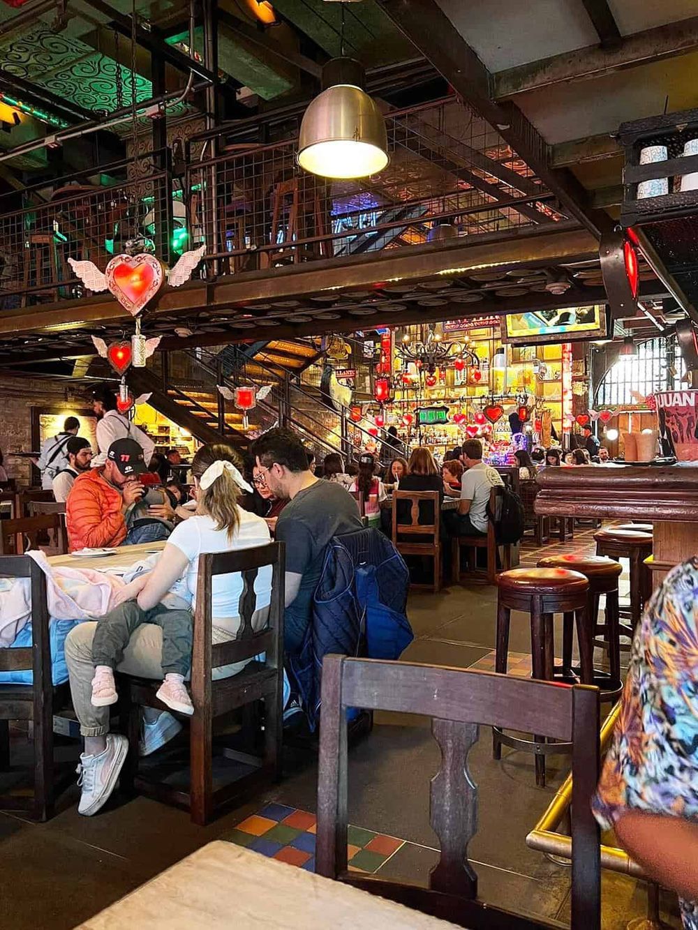 Colorful, lively restaurant interior with romantic heart-themed decorations and bustling guests.