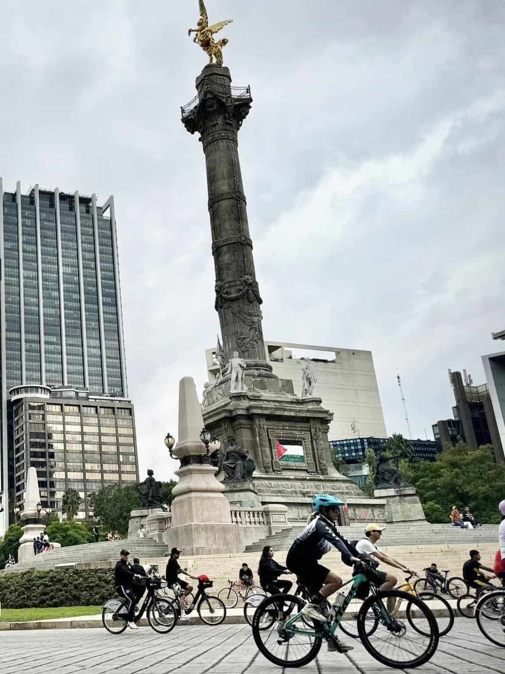 Elevador de Cibeles monument in Mexico City with cyclists and modern buildings in the background.