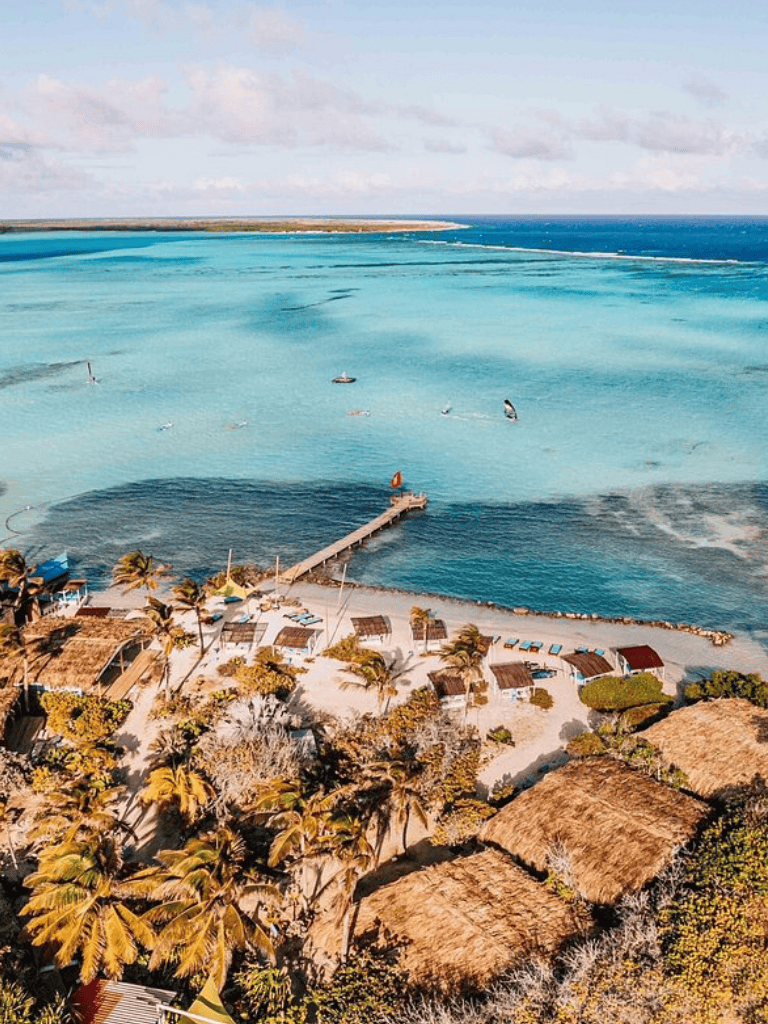 Azure beach and turquoise waters at QuestForDirections resort with palm trees and thatched roofs.