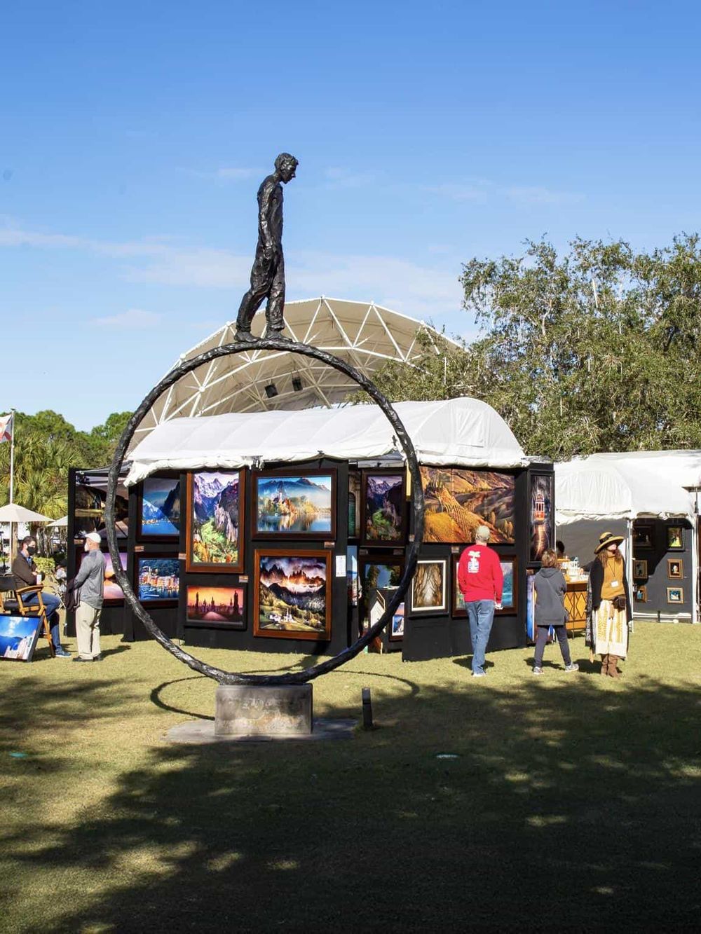 Colorful outdoor art display at a street fair or festival featuring paintings of natural landscapes and outdoor scenes.