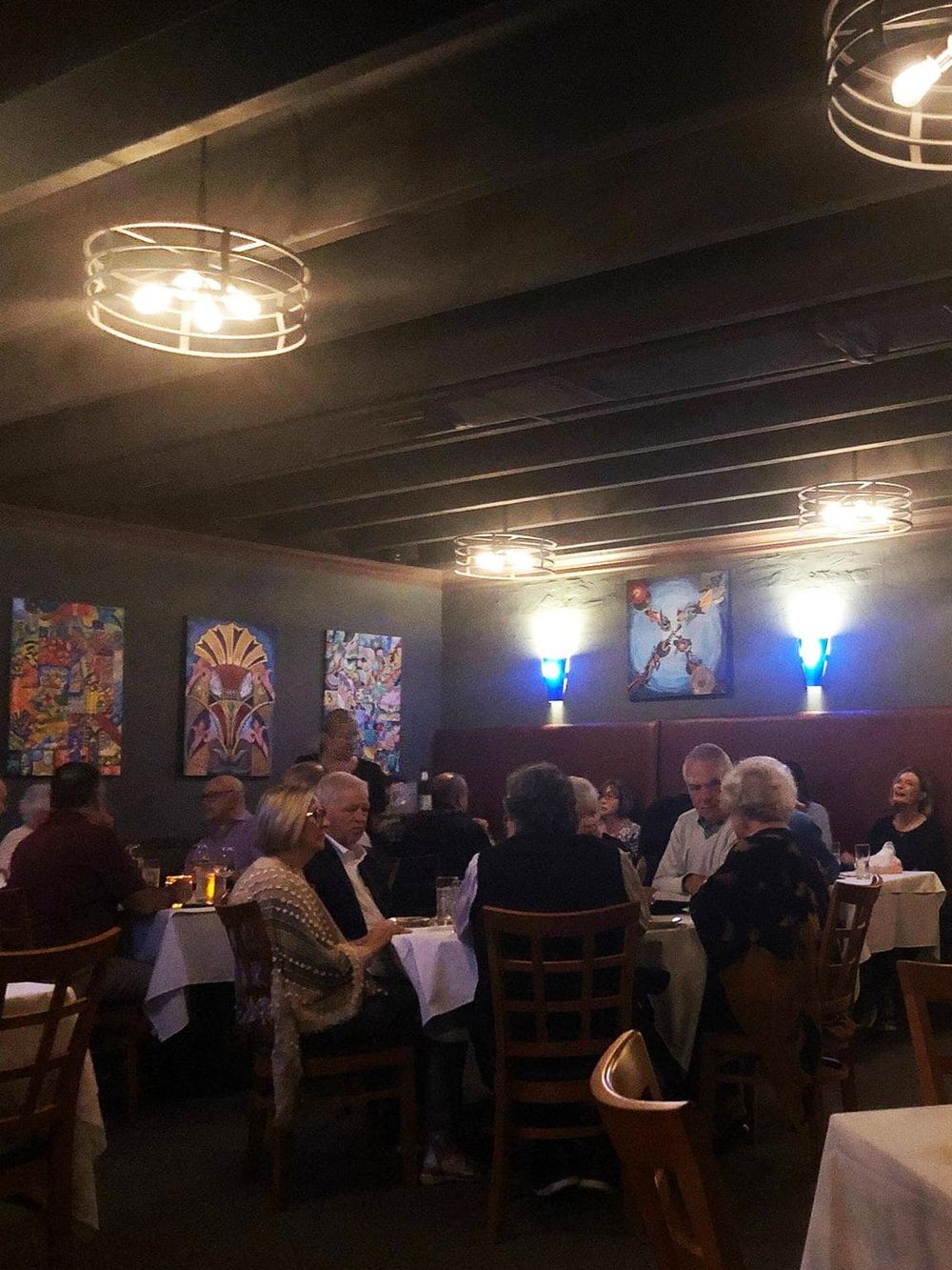 Cozy restaurant interior with dim lighting, colorful artwork, and guests enjoying dinner.
