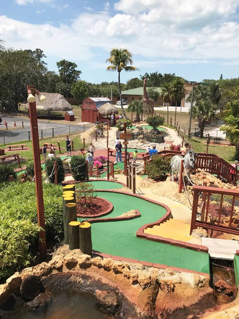 Colorful mini-golf course with animal sculptures, lush greenery, and visitors enjoying family fun at Quest for Directions.