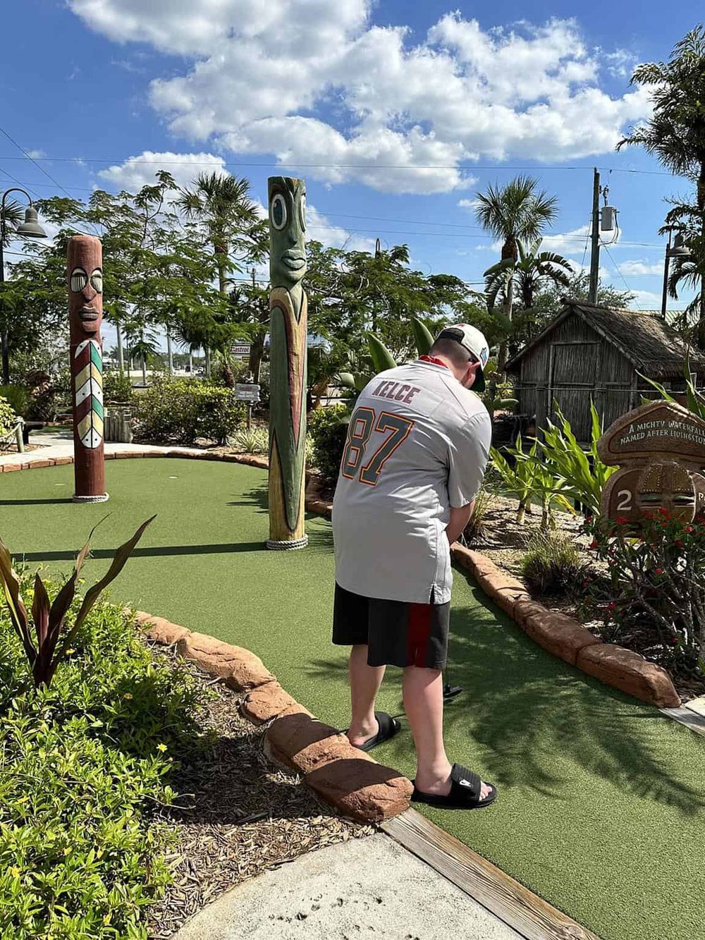Colorful Tiki statues at a mini-golf course in a tropical setting under a sunny sky.