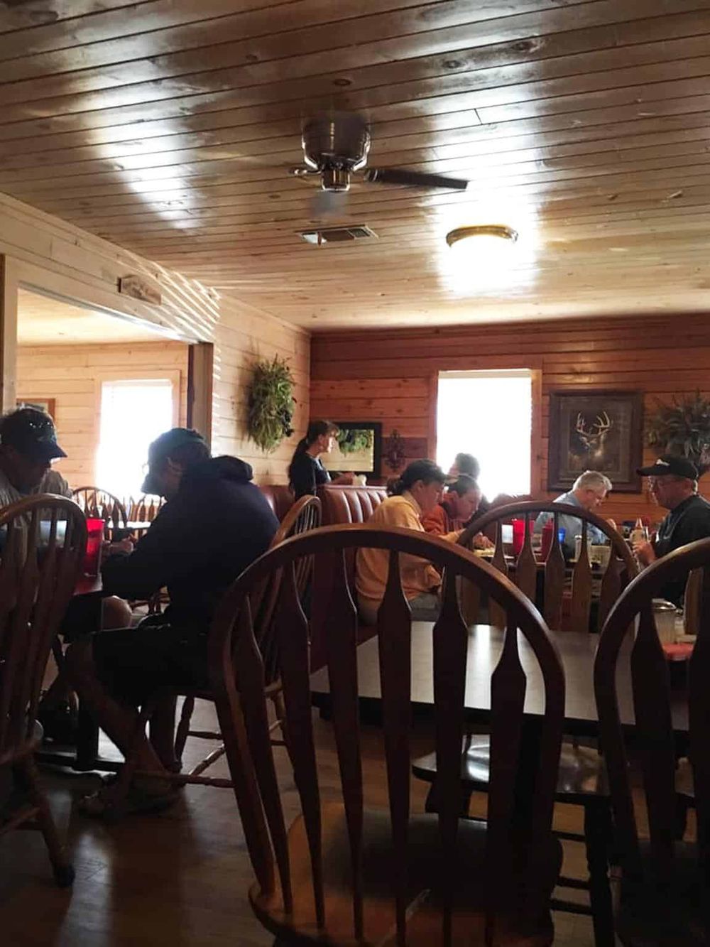 Cozy rustic restaurant interior with wooden walls and ceiling, people dining, and framed wildlife artwork.
