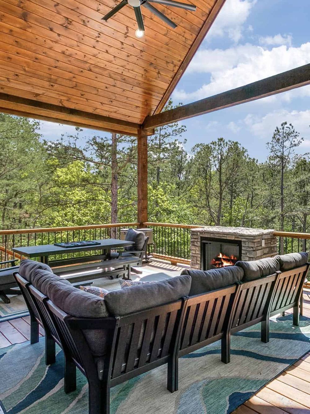 Cozy outdoor living area in a forest cabin with fireplace, comfortable seating, and breathtaking nature views.