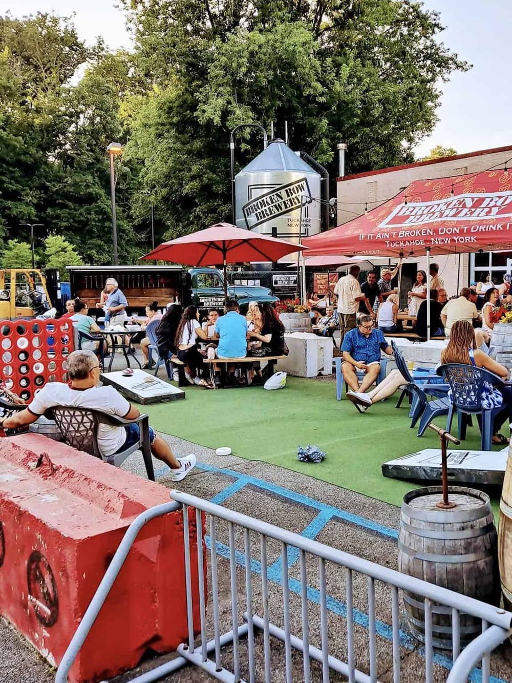 Outdoor beer garden with people enjoying drinks and food, featuring Broken Bow Brewery signage and vibrant, relaxed atmosphere.