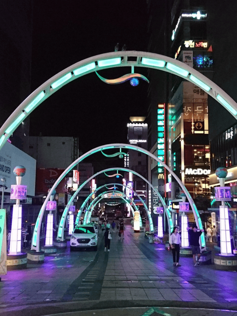 Bright neon street arches at night in a busy urban area with shops and restaurants, showcasing city nightlife and vibrant lights.