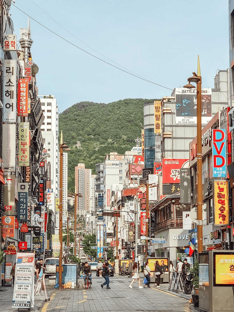 Colorful busy street in Seoul with vibrant signs and mountains in the background.