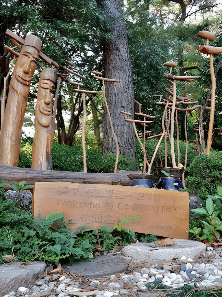 Colorful wooden sculptures and greeting sign at Cosuming Park surrounded by lush greenery and trees.