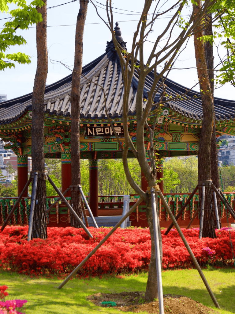 Colorful traditional Korean pavilion with vibrant flowers and lush greenery in the park.