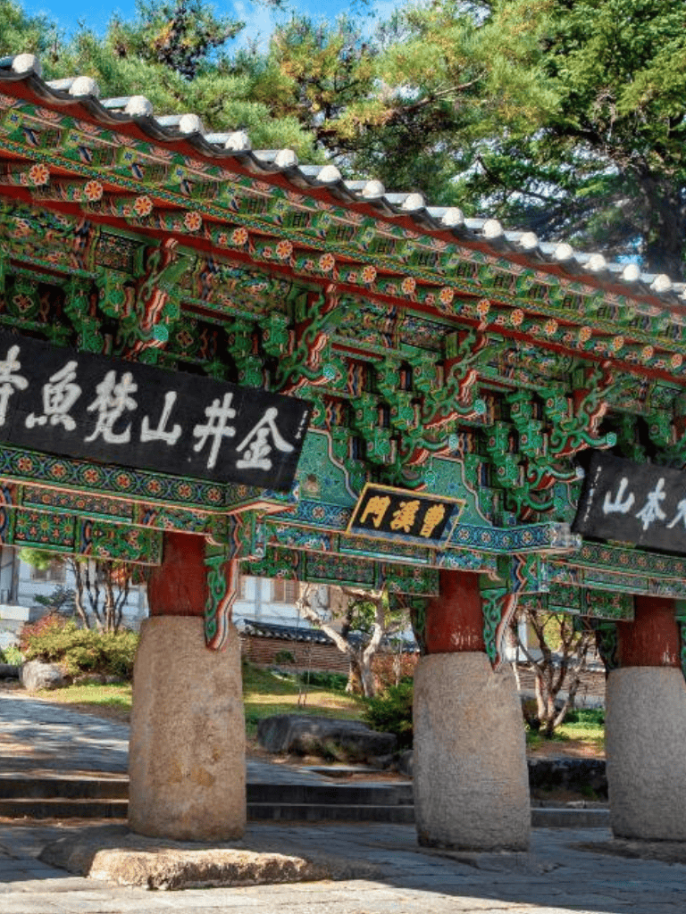 Colorful traditional Korean gate with intricate carvings and vibrant paintwork, set against lush greenery.