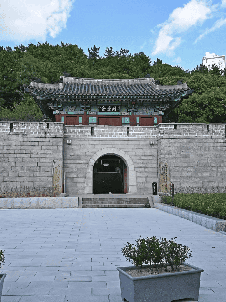 Ancient Korean temple gate surrounded by greenery and modern buildings in the background.