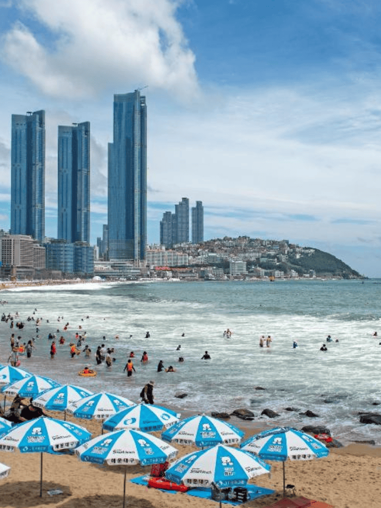 Beach cityscape with skyscrapers, blue umbrellas, and ocean waves, promoting QuestForDirections travel services.