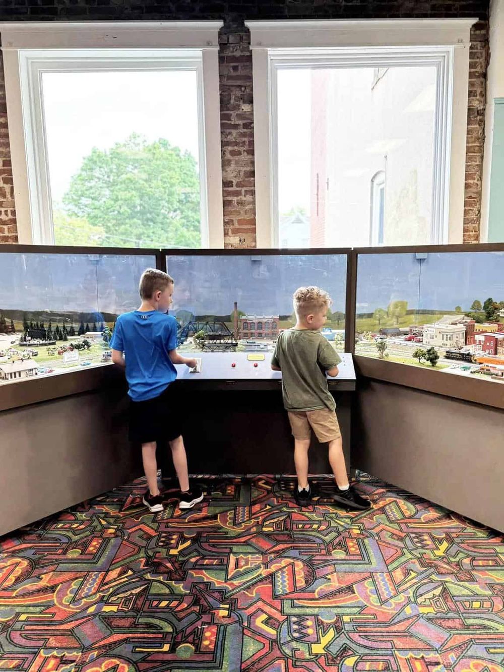 Children exploring a model train layout at QuestForDirections exhibit. Educational fun with detailed miniature cityscape.