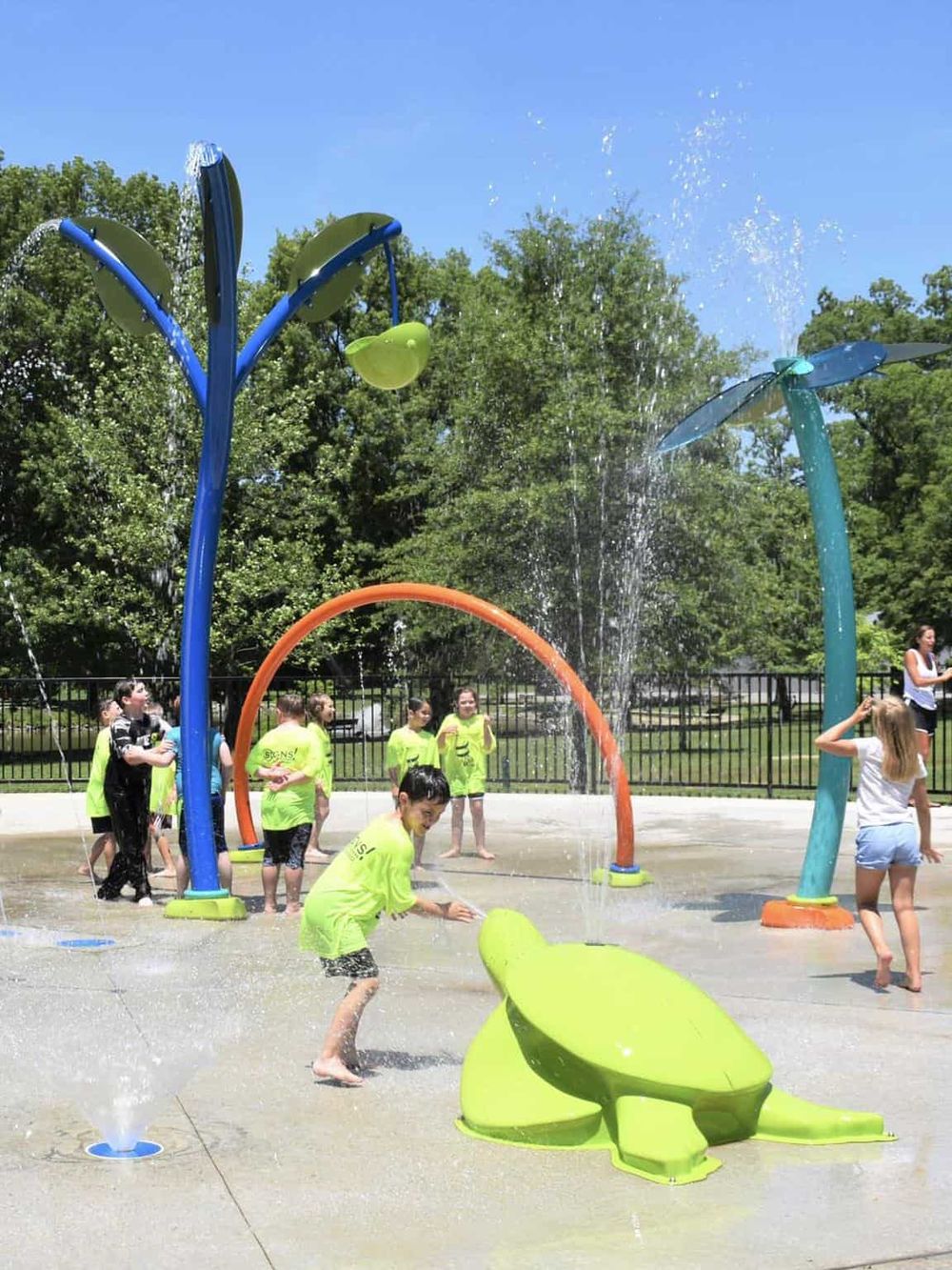 Colorful outdoor splash pad with children playing and water features, ideal for kids' fun and recreation.