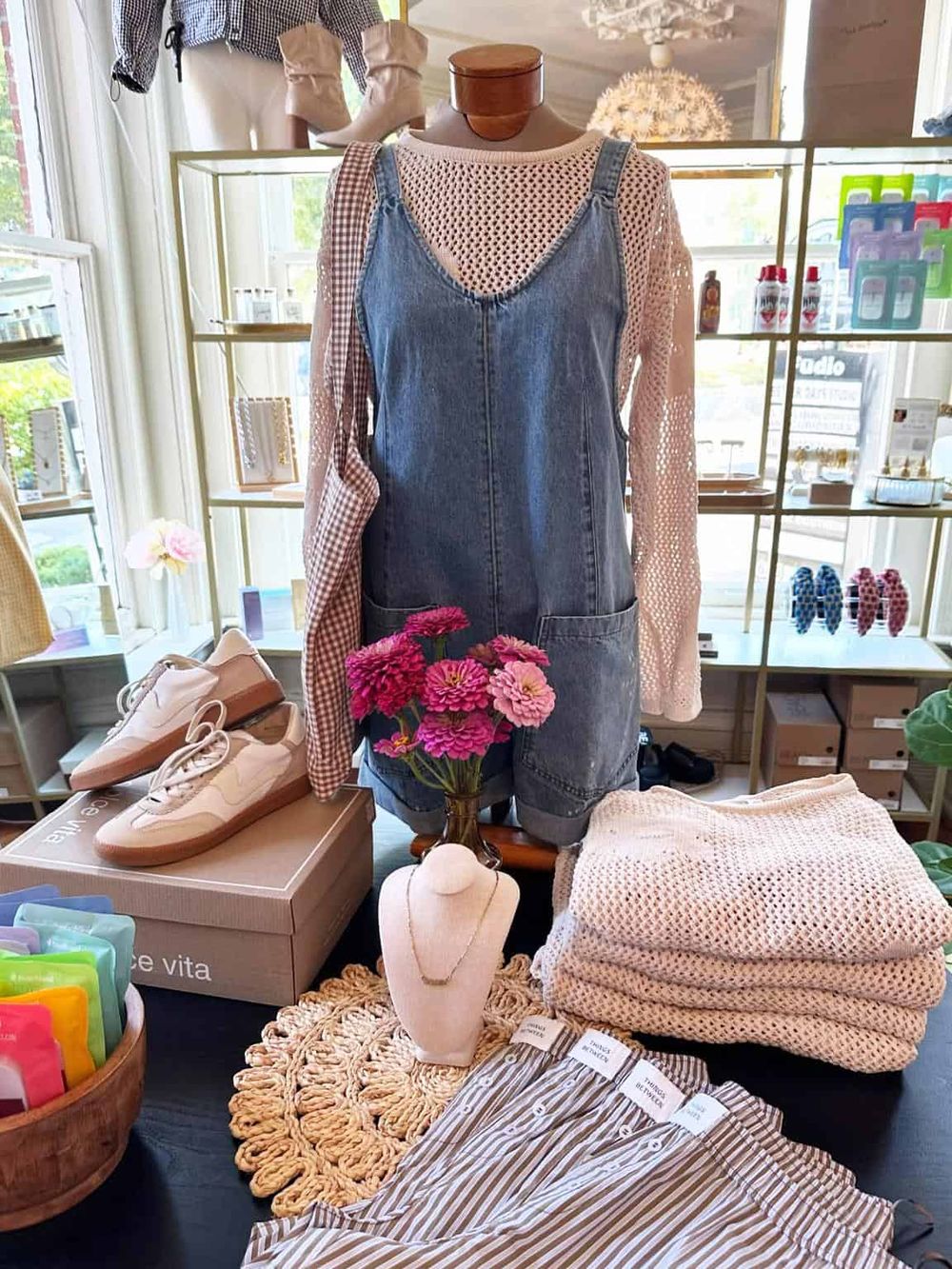 Stylish denim overalls layered with a pink crochet sweater, chic accessories, and trendy shoes in a boutique display.