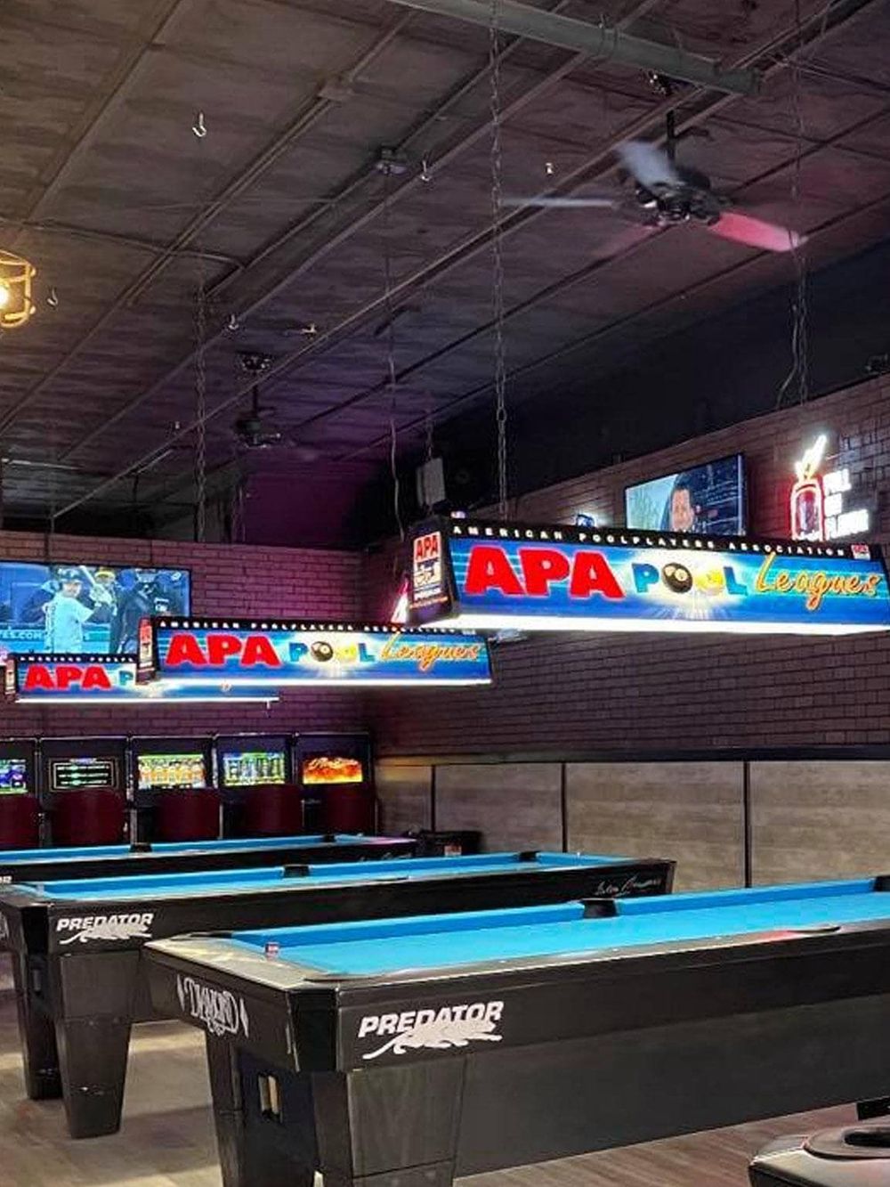 Bright indoor recreational space featuring APA Pool League signage and multiple pool tables for game nights.