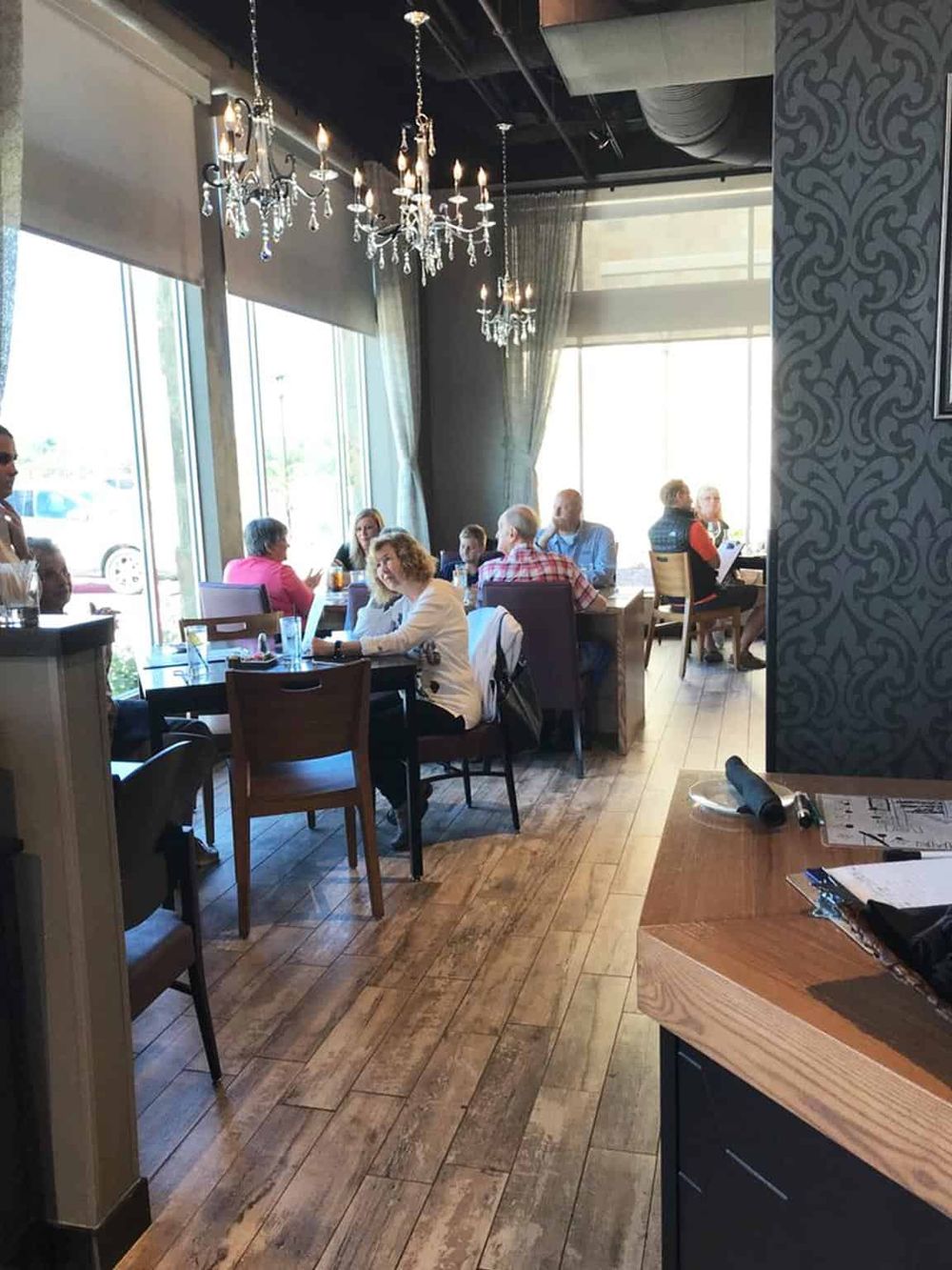 Stylish restaurant interior with chandeliers, large windows, and diverse patrons enjoying meals in a cozy setting.