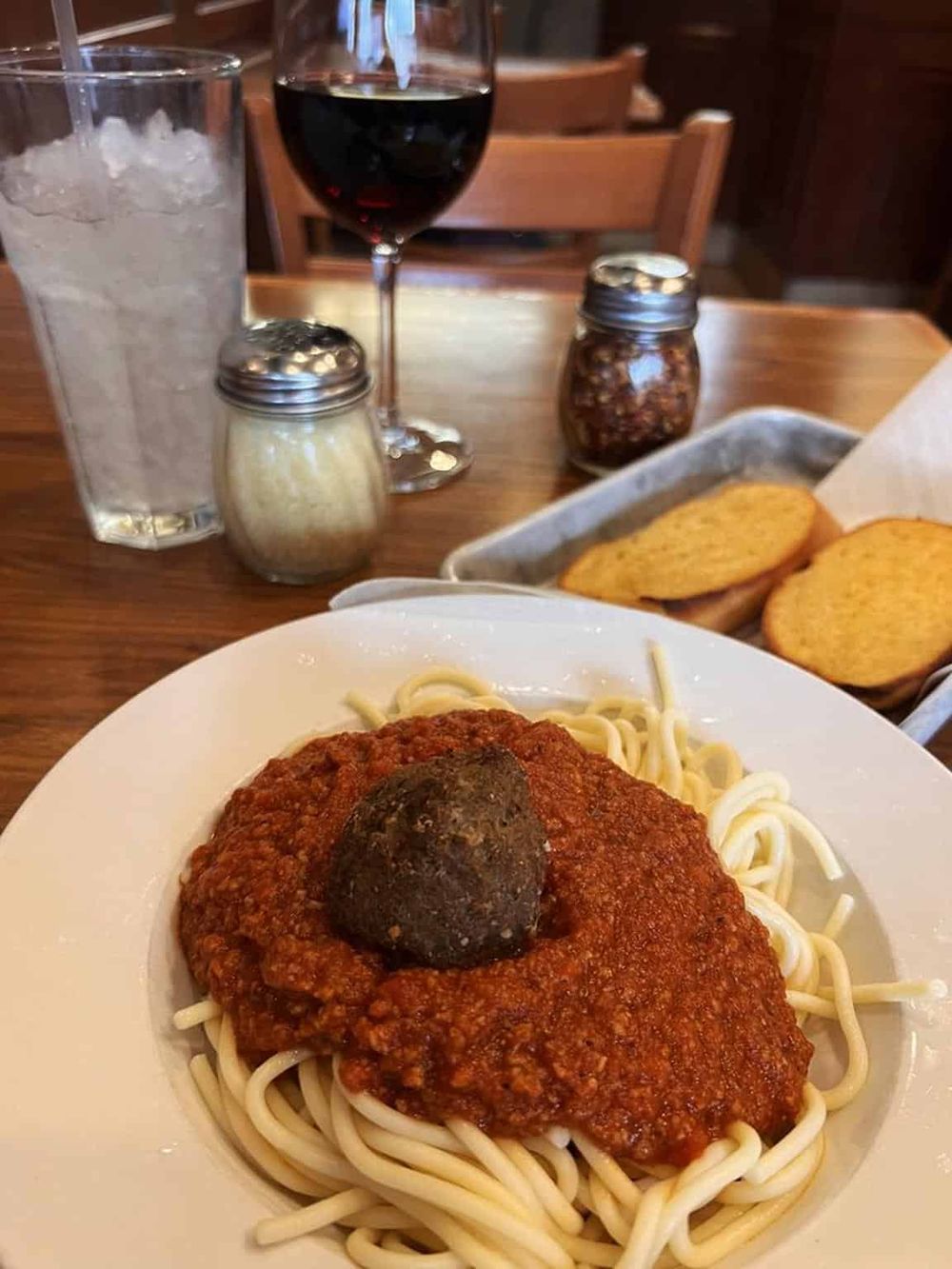 Creamy spaghetti with rich meat sauce and a meatball, served with garlic bread and beverages.
