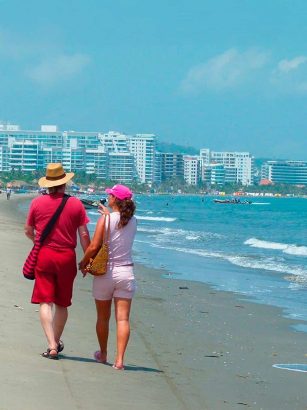Beach walk with women, ocean, and city skyline in the background, perfect for travel and tourism visuals.