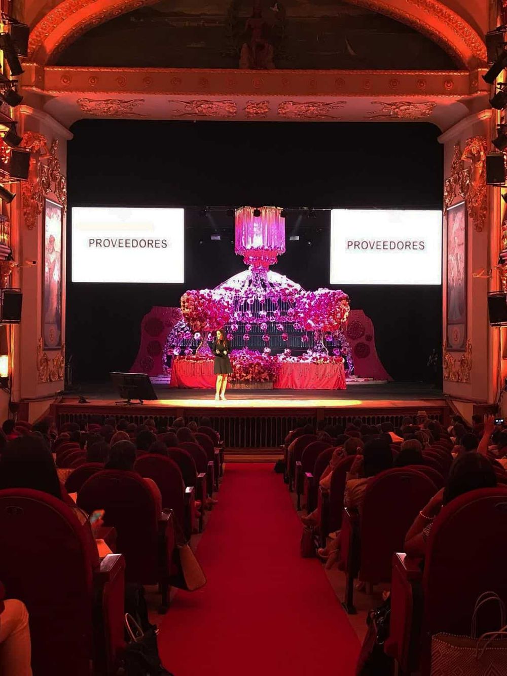 Elegant theater presentation with vibrant pink floral decor and large digital screens, showcasing event planning by QuestForDirections.
