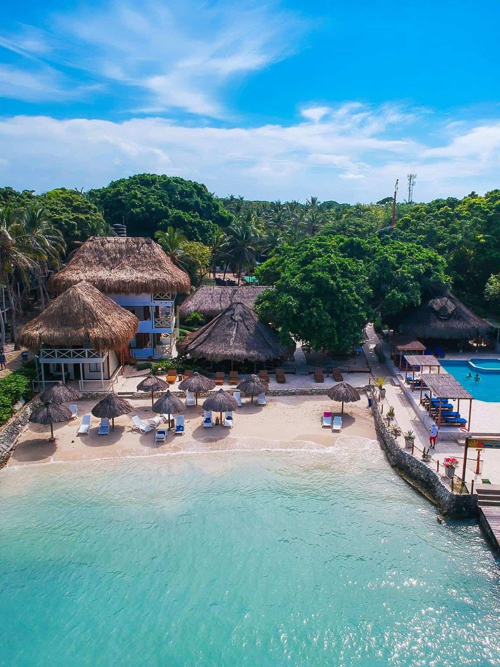Beautiful tropical beach resort with thatched-roof cabanas and clear turquoise waters.