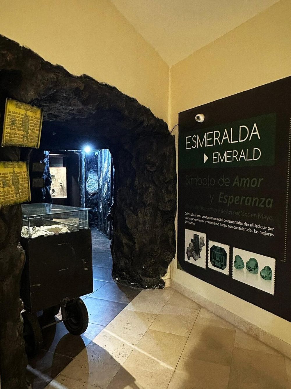 Vibrant emerald gemstone display at Quest for Directions museum, symbolizing love and hope, in a dark stone cave setting.