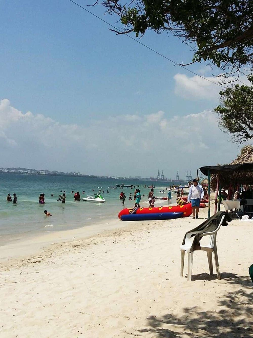 Vibrant beach scene with swimming, jet skiing, and sunbathing under sunny skies, perfect for vacation and leisure.