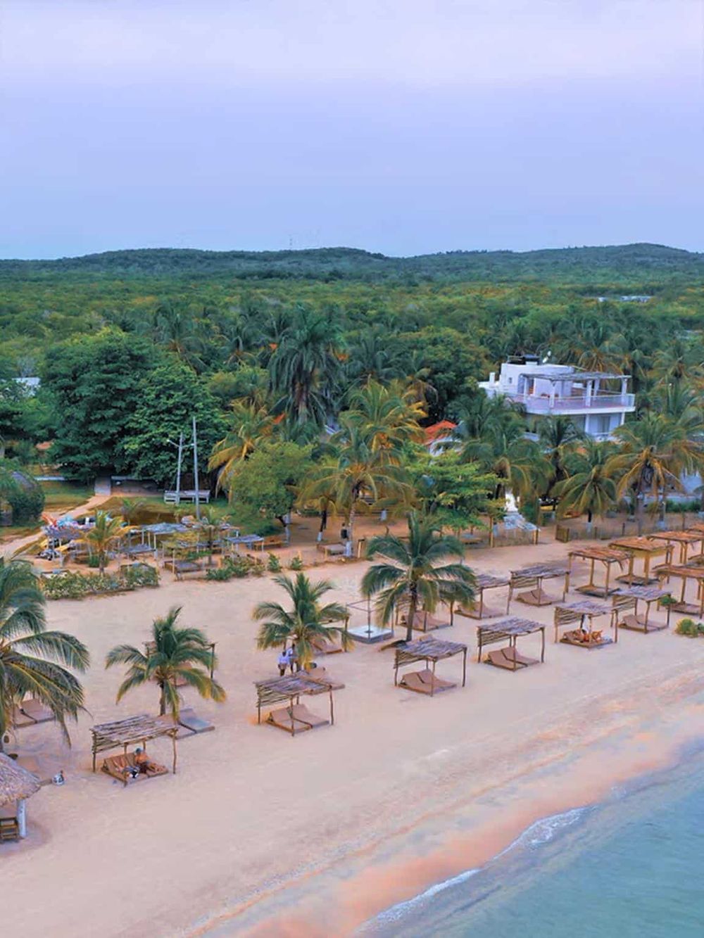 Beach with palm trees and beachfront cabanas at sunset, tropical vacation destination.