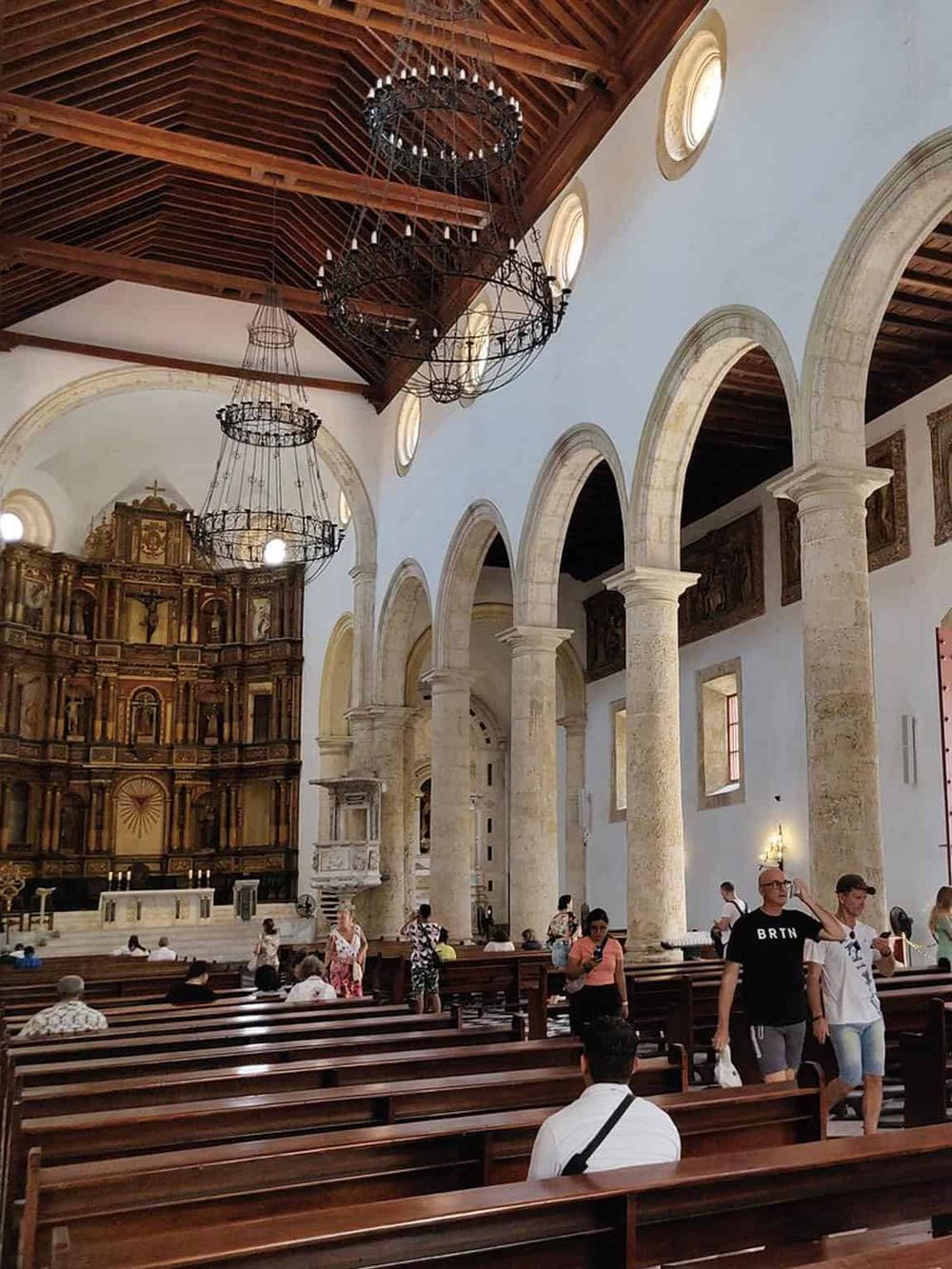 Intricate church interior with stone arches, wooden ceiling, and chandeliers, showcasing historic architecture.